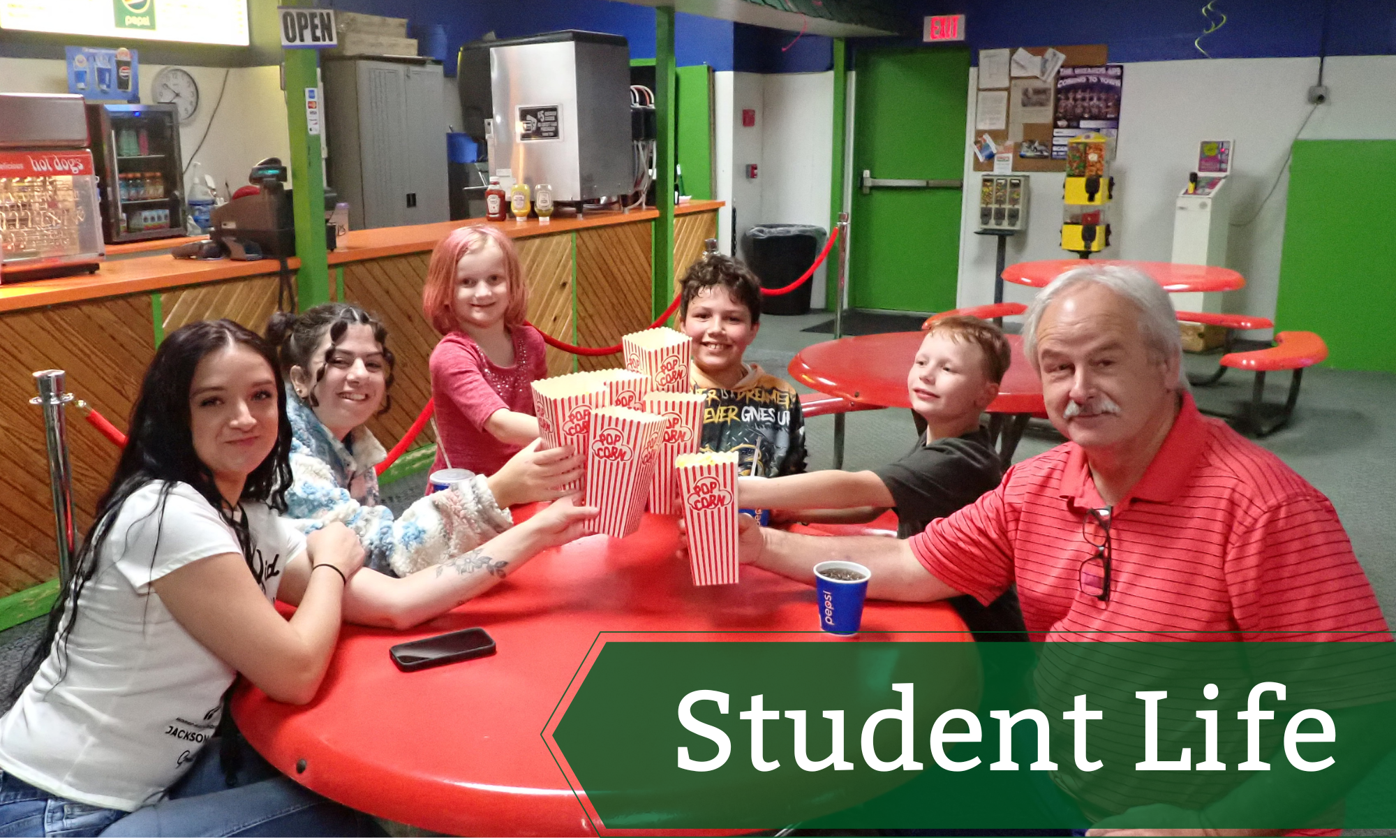 Photo of a group of students and staff at a roller rink sitting at a round table holding buckets of popcorn.