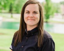 White female with brown medium length hair wearing a dark blue button up shirt.