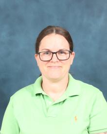 Photo of a white woman with brown hair wearing glasses and a green polo shirt.