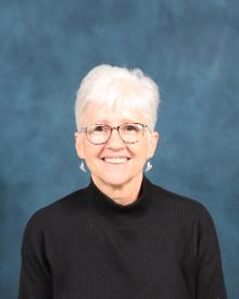 Older white female with white hair wearing glasses and a black turtle neck.